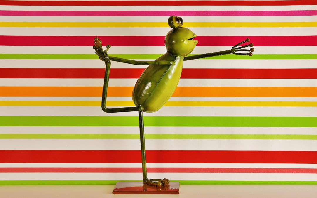 Image of a metal sculpture of a green frog doing a yoga pose against a horizontally striped rainbow background