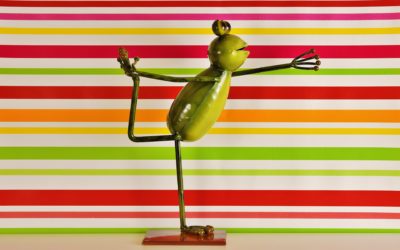 Image of a metal sculpture of a green frog doing a yoga pose against a horizontally striped rainbow background