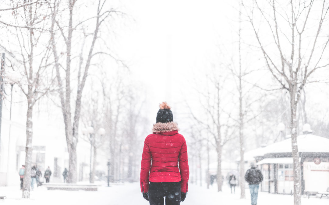 Woman standing in the middle of the park in snowy weather wearing a read coat and black pants