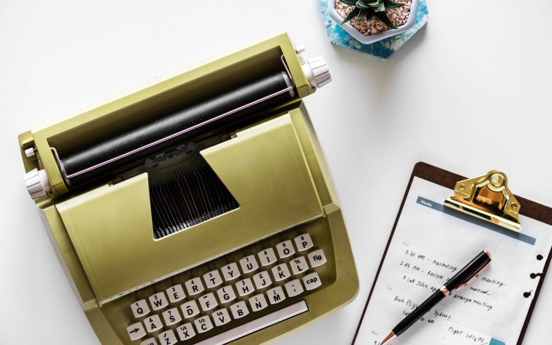 Photo of a gold typewriter and a notepad on a brown clipboard with writing on it and a pen on top
