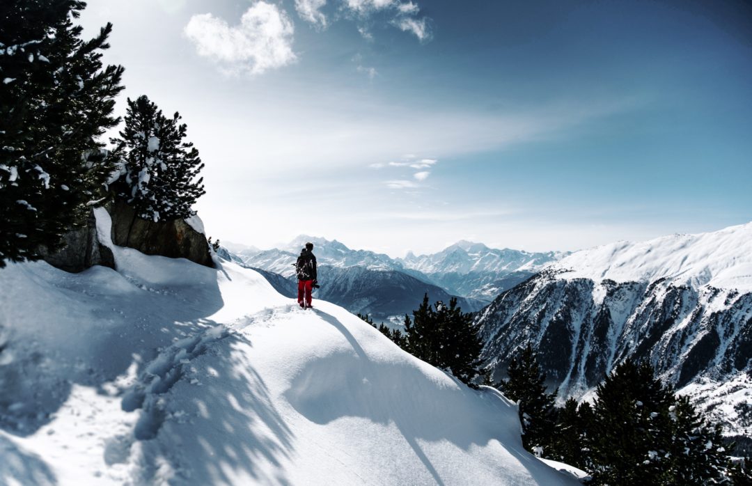 A person walking on a snow covered mountain overlooking a valley with fresh footprints behind them