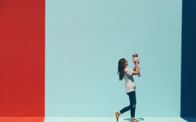 A Woman walking and holding an infant against a red, light blue and dark blue background