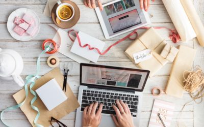 Photo of laptop with many different books, gifts and other items around it indicating busyness