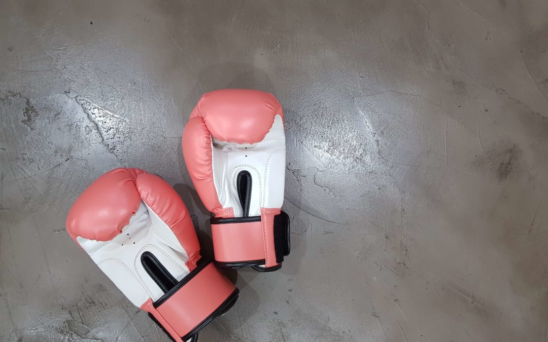 Image of a pair of pink and white boxing gloves laying on a grey concrete floor