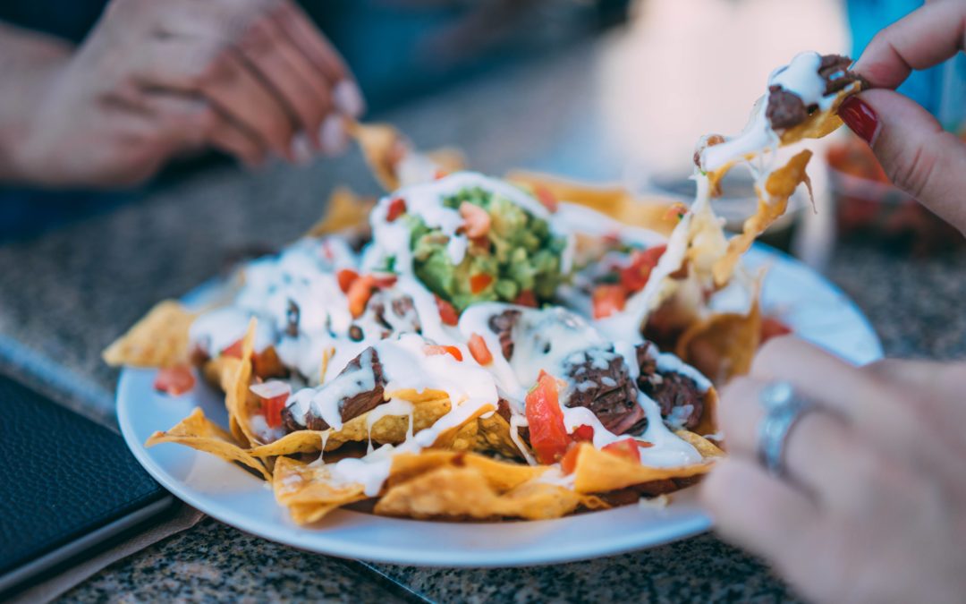 Photo of hands reaching for a plate of cheesy nachos with meat, onions, and peppers on top