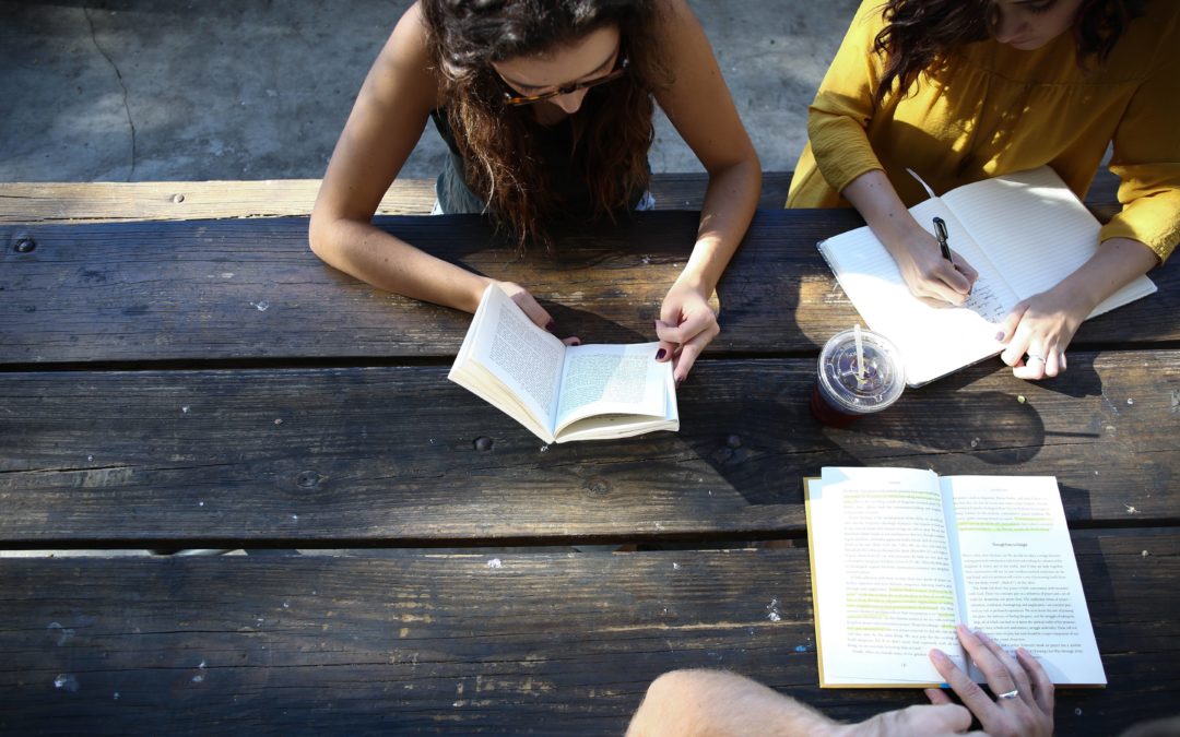 Photo from above of three girls reading books together sitting at a picnic table