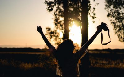 Woman facing away from camera with arms up towards the sunset