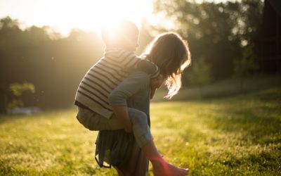 Image of a woman with brown hair piggybacking a child with the sun brightly shining