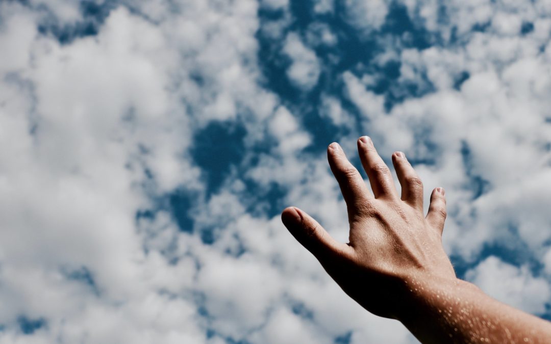 Image of a man's hand reaching toward the cloudy, blue sky