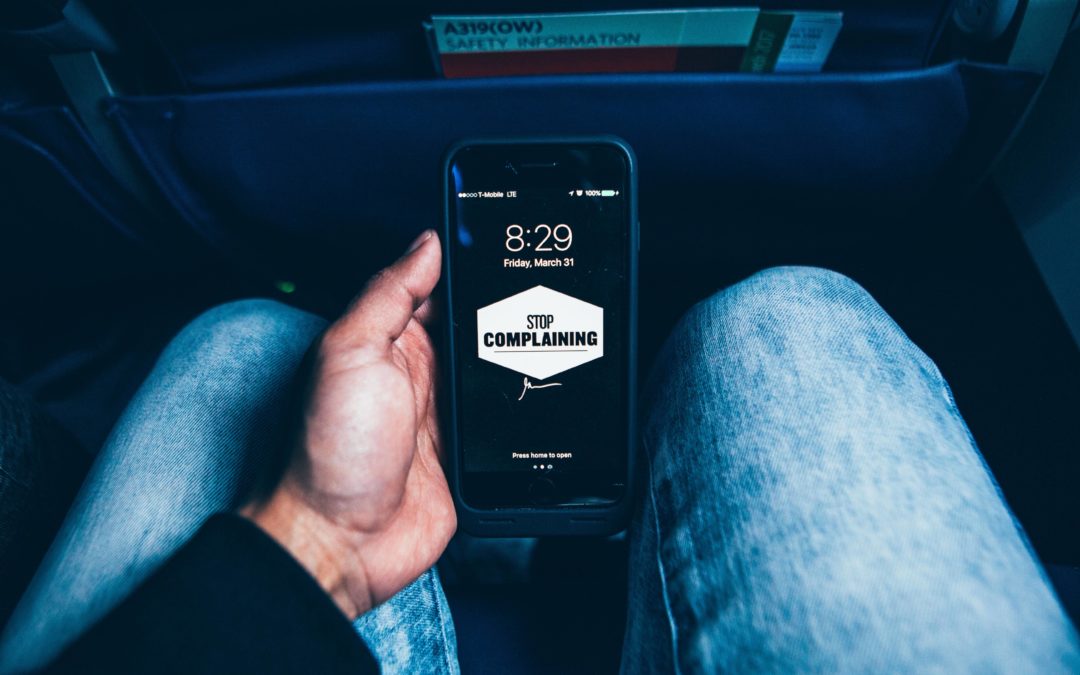 Image of a man holding his cell phone with the words "Stop Complaining" on the screen