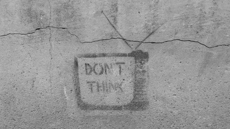 An image of a painting on a cement wall that says "Don't think" inside of a television