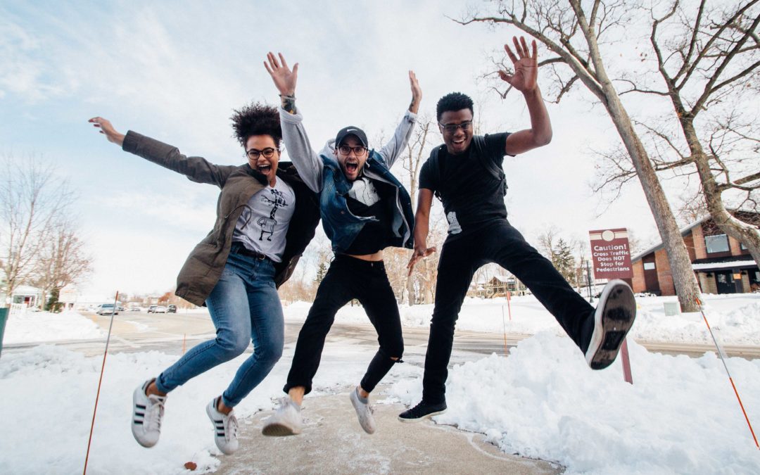 Photo of three high school age kids walking down the sidewalks with their hands up in the air looking excited