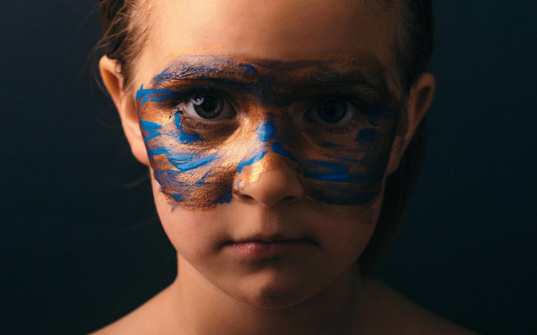 Photo of a young girl with multi-coloured face paint in the shape of a superhero mask