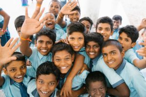 Photo of many boys hugging and smiling of the camera in light blue school uniforms