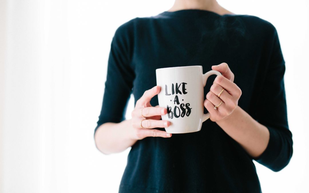 A woman in a black sweater holding a white mug with black writing that says: 'Like a boss" on it