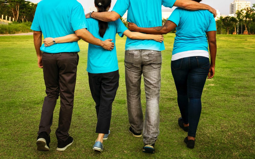 Photo of four people wearing turquoise shirts and jeans walking away with their arms around each other