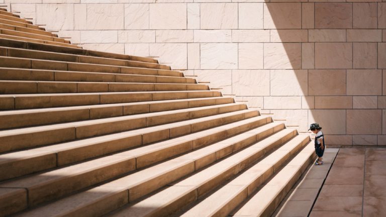 Small boy looking down at the first step at the bottom of a very long staircase