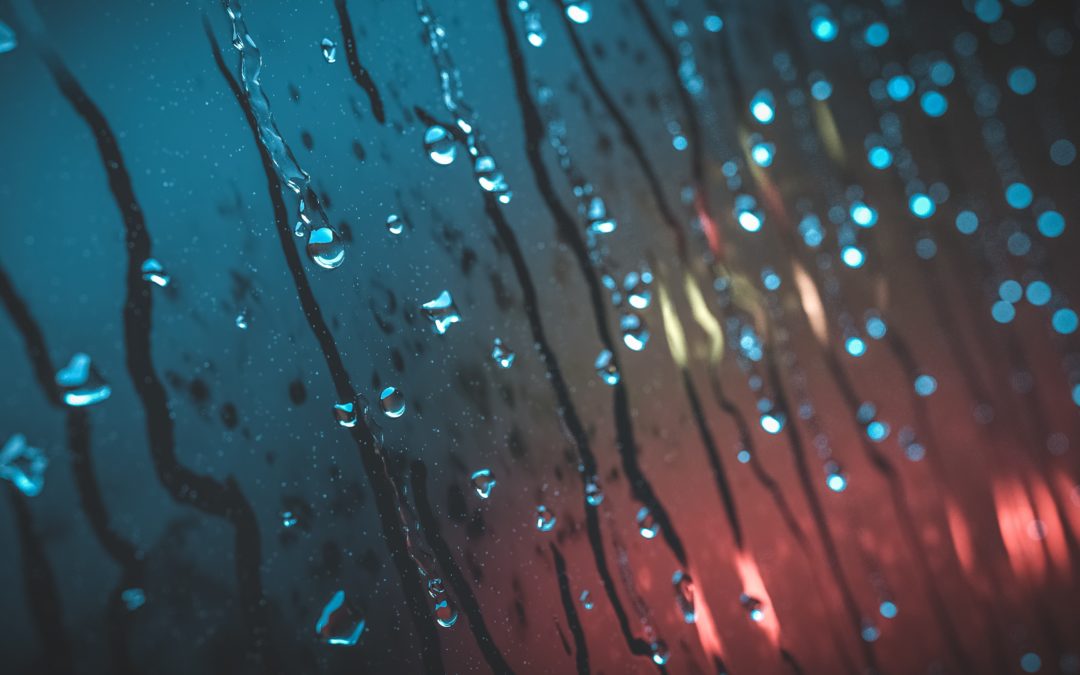 Raindrops running down a window with red car lights behind
