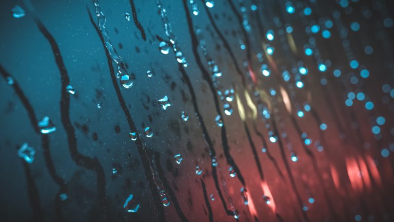 Raindrops running down a window with red car lights behind