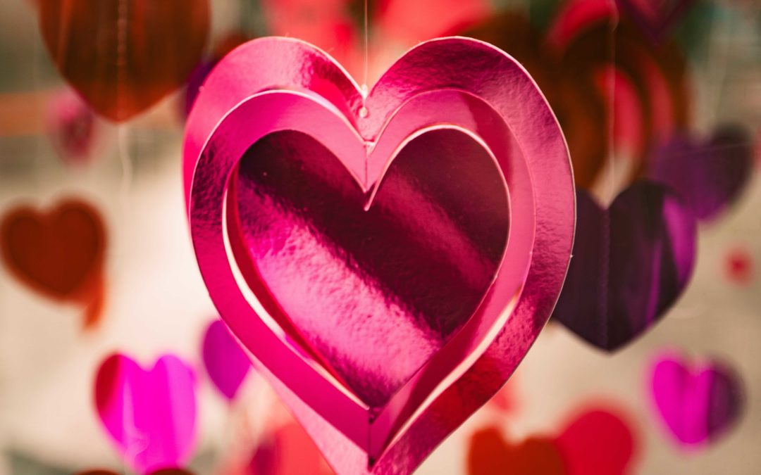 Photo of a hanging pink shiny paper heart with red and pink heart in the background