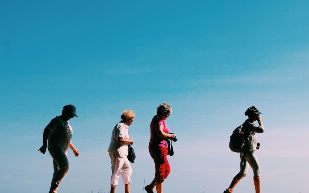 Four women walking one after another against a blue sky backdrop