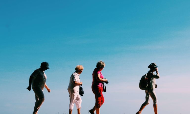 Four women walking one after another against a blue sky backdrop