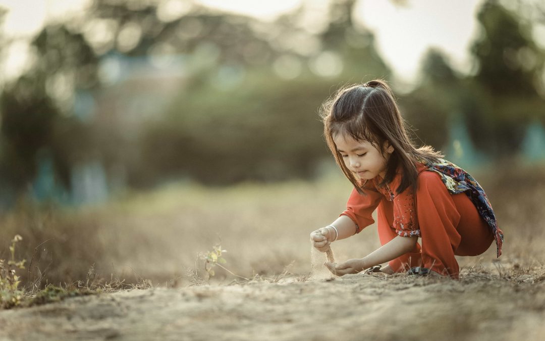 Little Asian girl crouching down and playing with sand