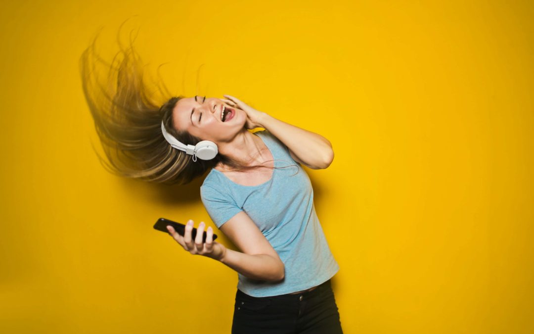 Woman singing to perform under pressure with headphones on and eyes closed against a yellow backdrop