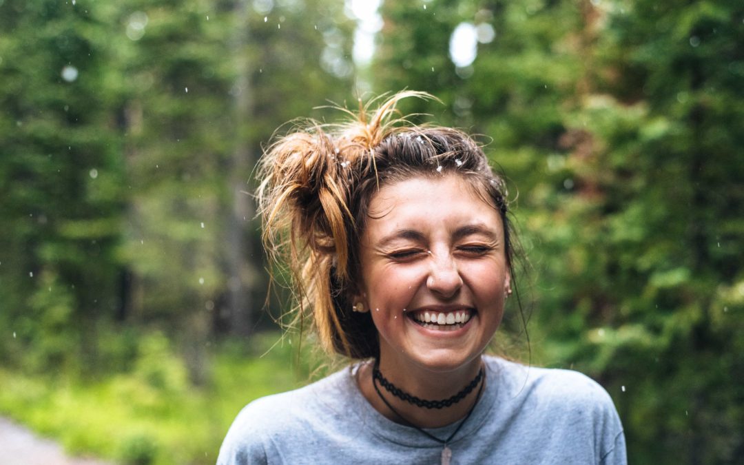 Photo of a woman laughing with a green backdrop of trees behind her