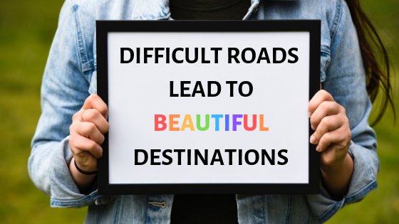 Woman holding a sign that says "Difficult roads lead to beautiful destinations"