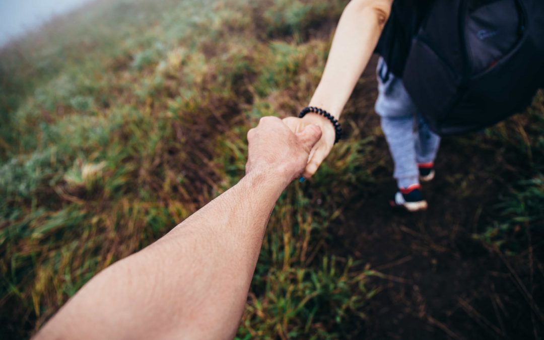 One person reaching out to hold another person's hand for support while hiking