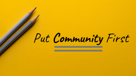 The words Put Community First written on a yellow background with two grey pencils above