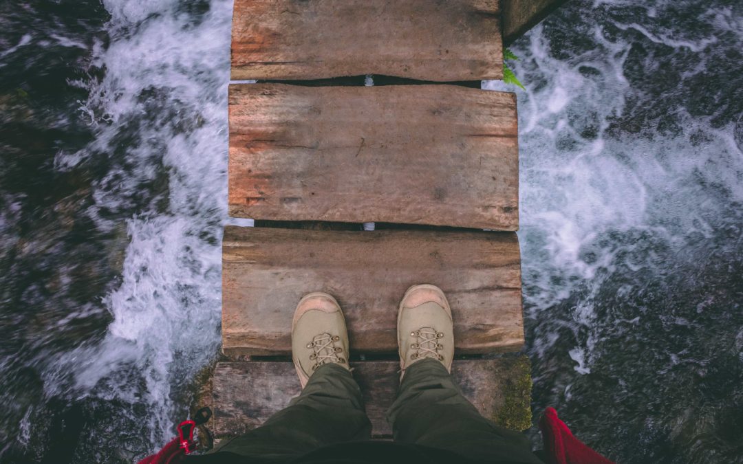 Photo looking down on a person's shoes standing on a narrow bridge over rough water