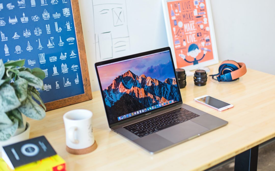 Image of a laptop on a desk with a mug, book, poster and plant
