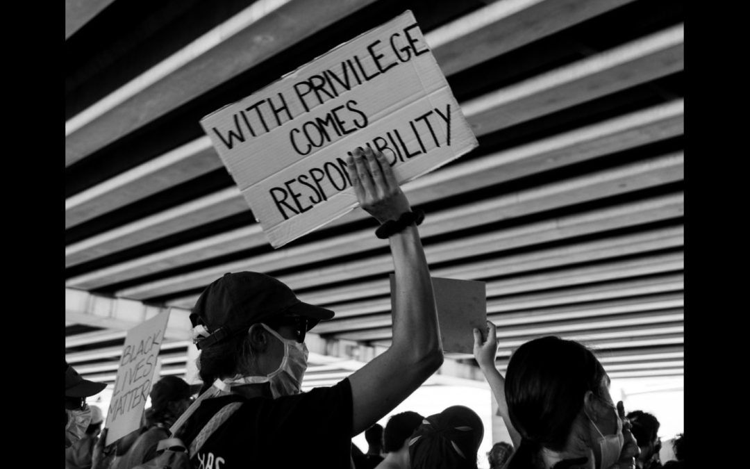 White man wearing a face mask holding up a sign at a protest that says: "With privilege comes responsibility"